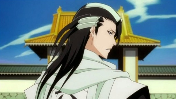 homem branco de cabelos pretos longos, com enfeites metálicos no cabelo. Ele parece estar em frente a um templo